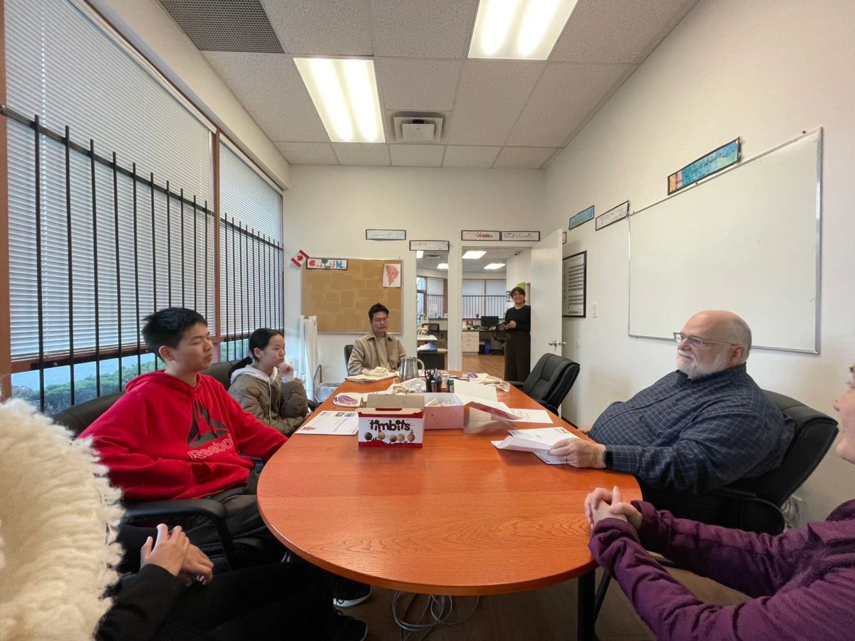 Group of people in a meeting room around a wooden table with papers and snacks.